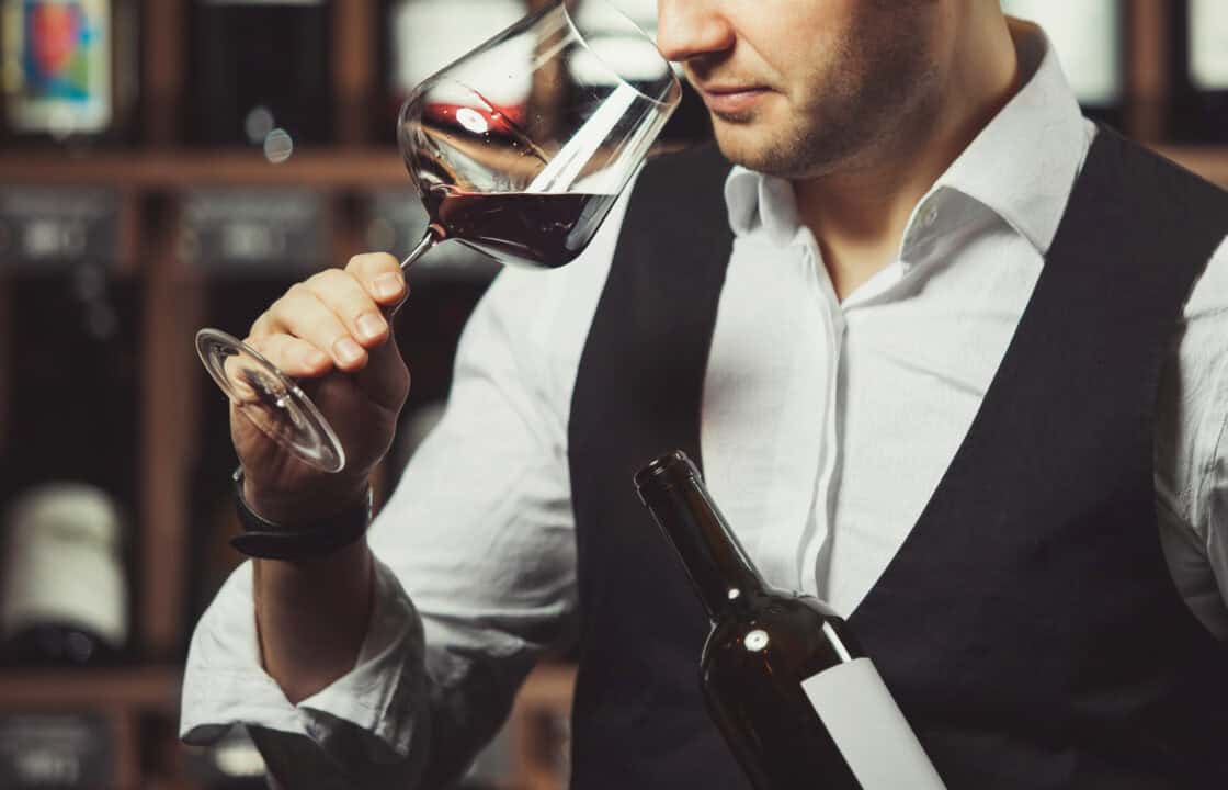 Close-up snimak mladog somelijea koji miriše crno vino na pozadini vinskog podruma. Stručnjak u oblasti alkoholnih pića.