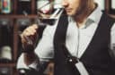Close-up snimak mladog somelijea koji miriše crno vino na pozadini vinskog podruma. Stručnjak u oblasti alkoholnih pića.